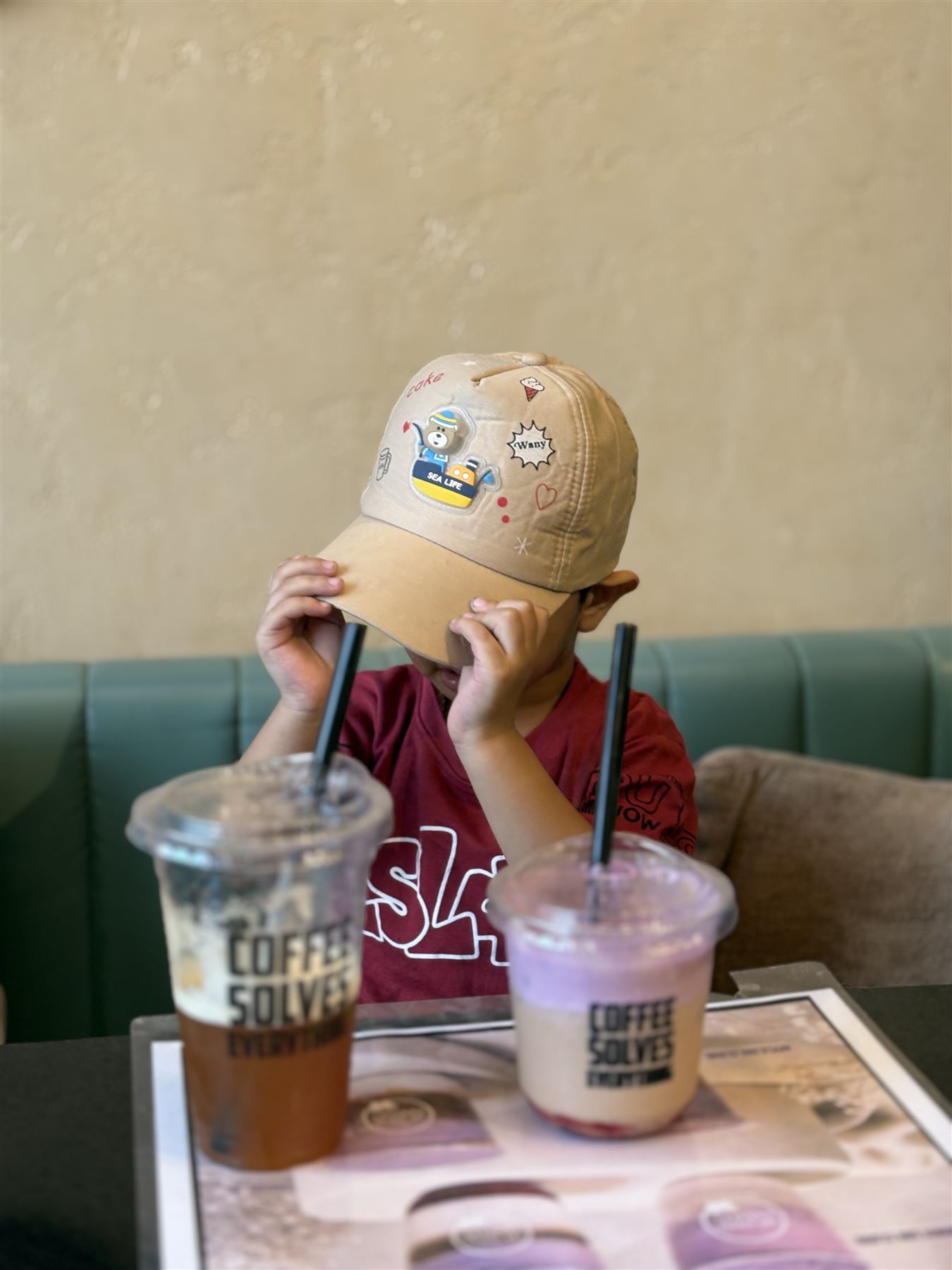 A young guest peeking from under his cap behind two drinks